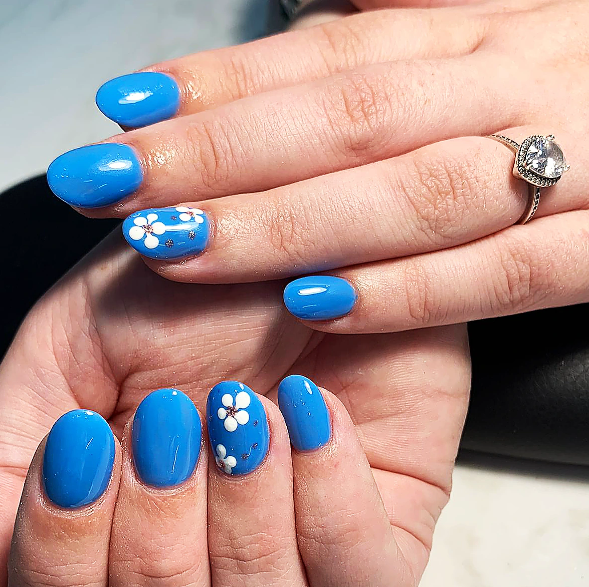 Short bright blue gel nails with white flower art on two accent nails.