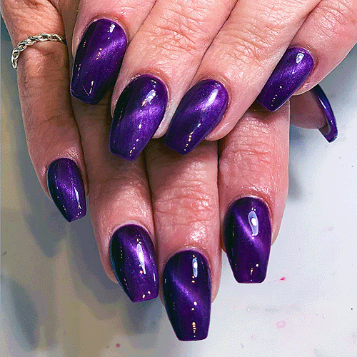 Close-up of hands with glossy, deep purple metallic manicure on square-shaped nails.