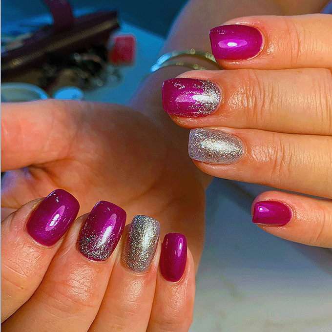Close-up of hands displaying nails with shiny purple and silver glittery nail polish.