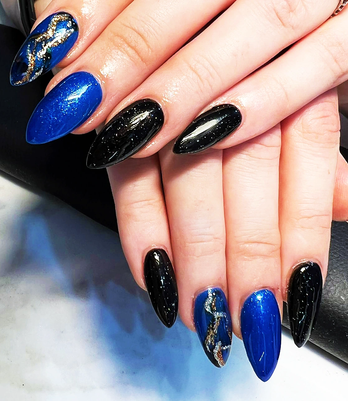 Almond nails in cobalt blue and black with gold foil accents.