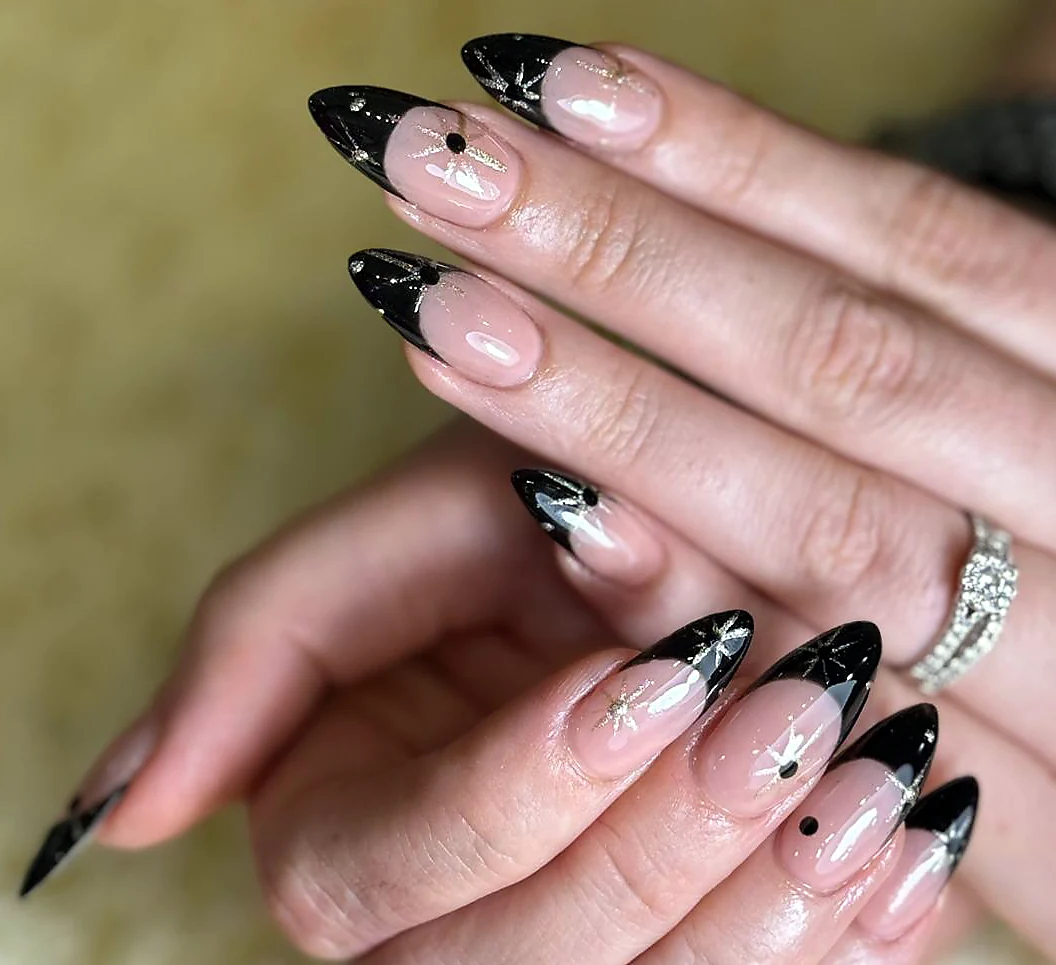 Almond nails with a nude base, black French tips and small black dot details.