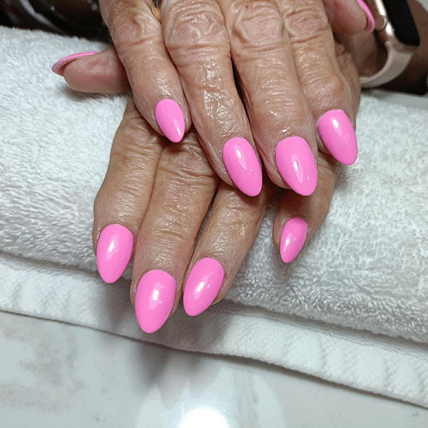 Hands with long almond-shaped acrylic nails in pink and purple glitter, one pink nail featuring a black heart design.
