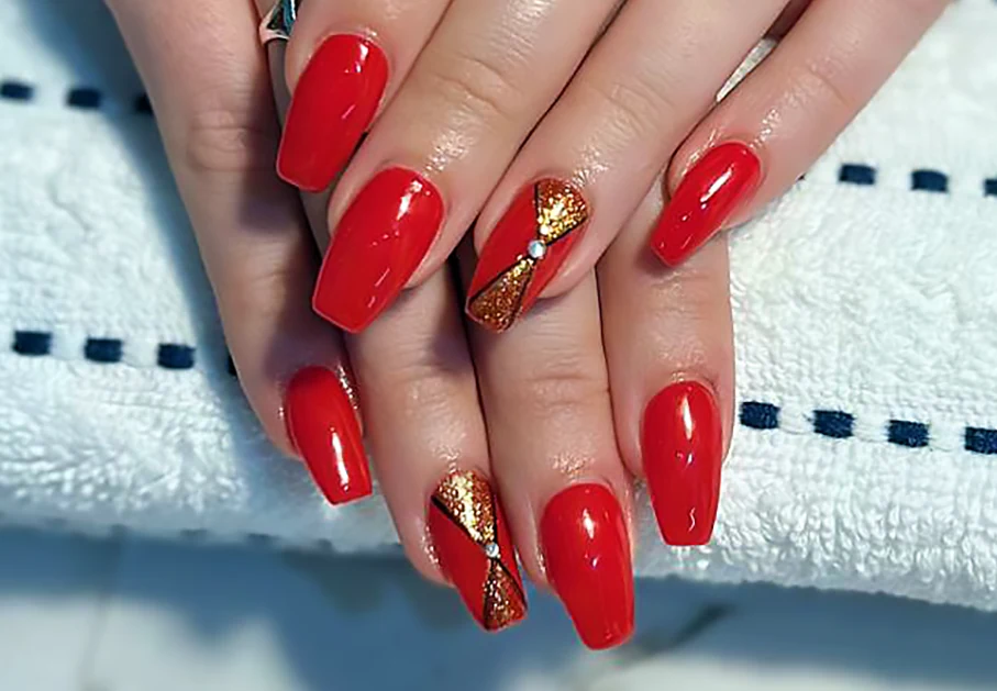 Coffin nails in glossy red with gold glitter bow designs on two accent nails.