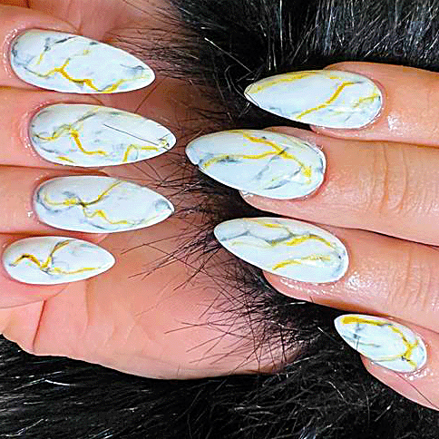 Hands with long almond-shaped nails featuring white marble nail art patterns with gold veining.