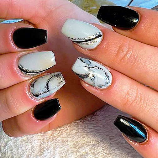 Hands with acrylic nails featuring a black and white marble design and solid black nails.