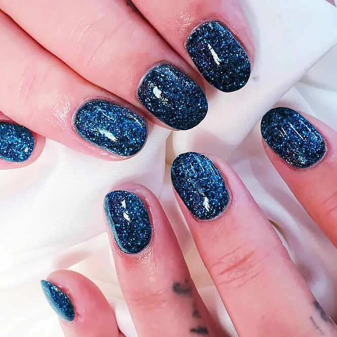 Short natural nails with a dark blue sparkle gel manicure.