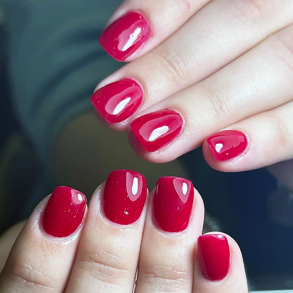 Short natural nails with a glossy red gel manicure.