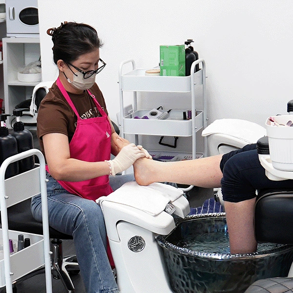 Nail technician giving a client a spa pedicure at a pedicure chair.